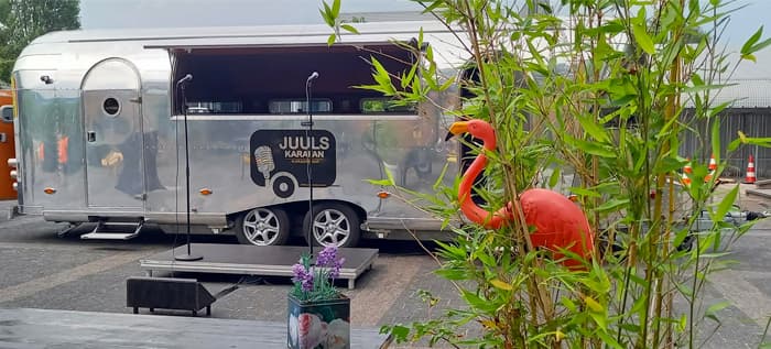Zilveren Karafan met het opschrift Juuls Karafan Karaoke Bar, open zijklep en een podium met twee microfoons